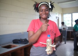 Photo of a female student holding a bird feeder made from a plastic bottle and wooden spoons.