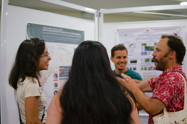 Group of 4 people- 2 males and 2 females speaking to each other next to a scientific poster.